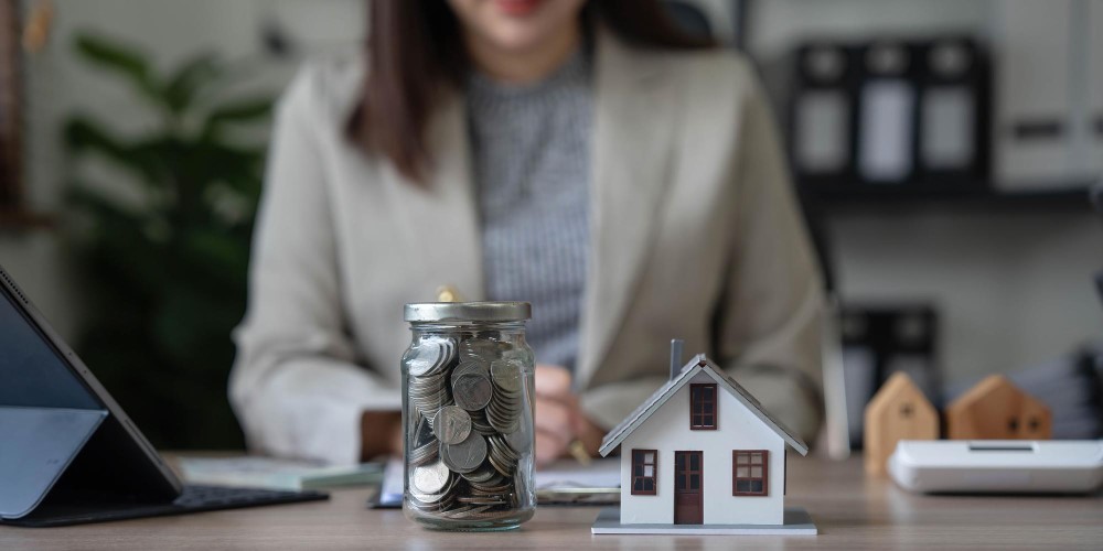 Woman at a desk with a jar of coins and a model house