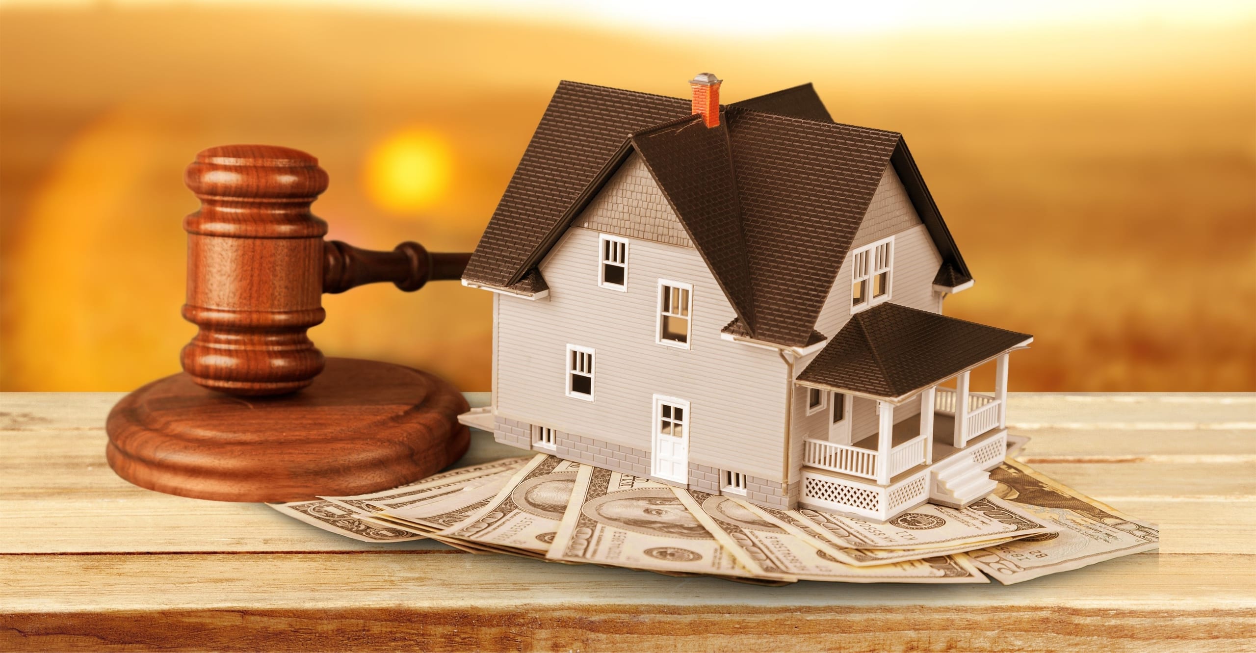 Gavel, model house, and dollar bills on a wood table
