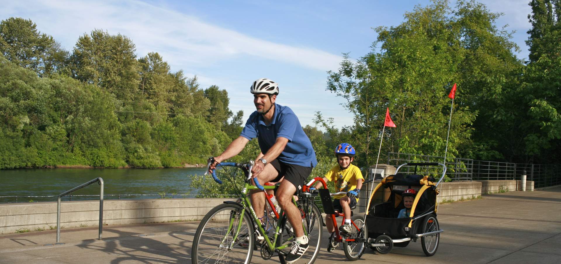 Man and two children biking along a river path