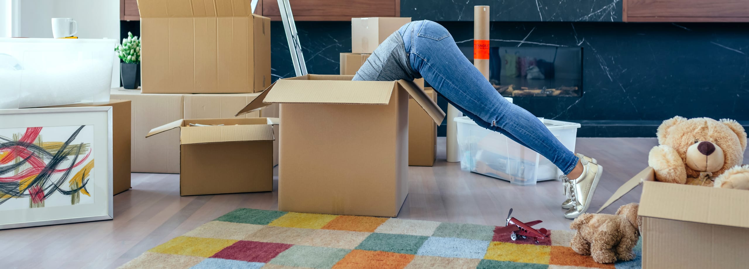 Person in jeans diving into a moving box in a room full of boxes