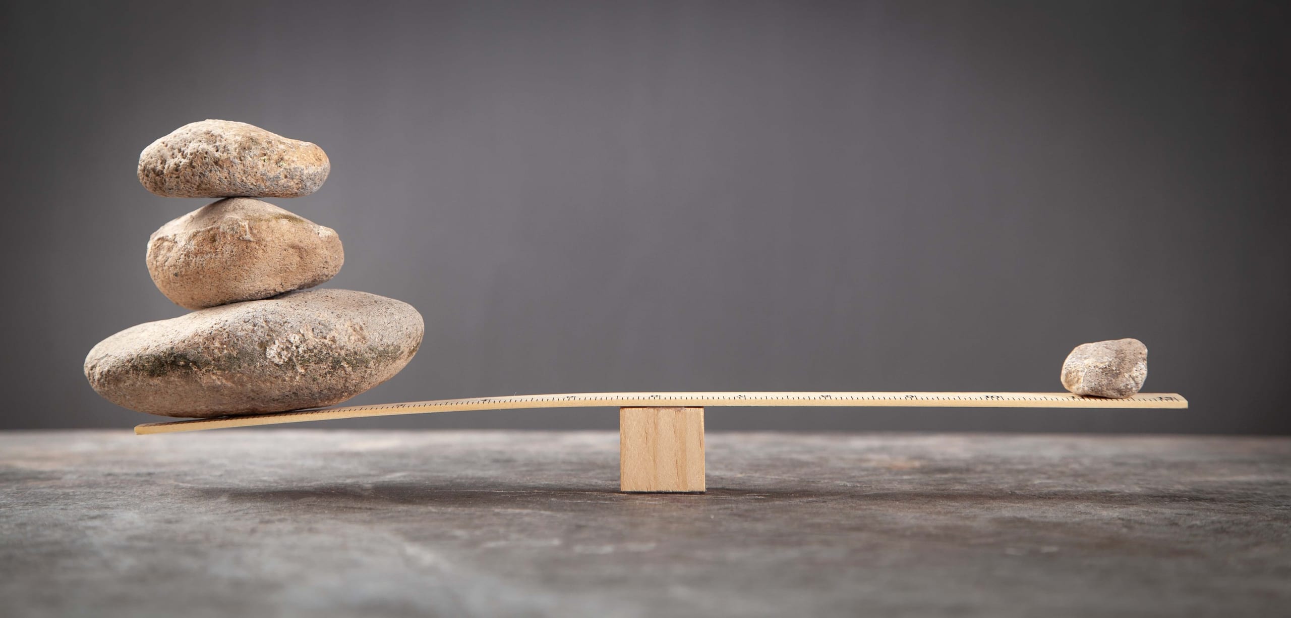 Stacked stones on one end of a wooden balance and a small stone on the other