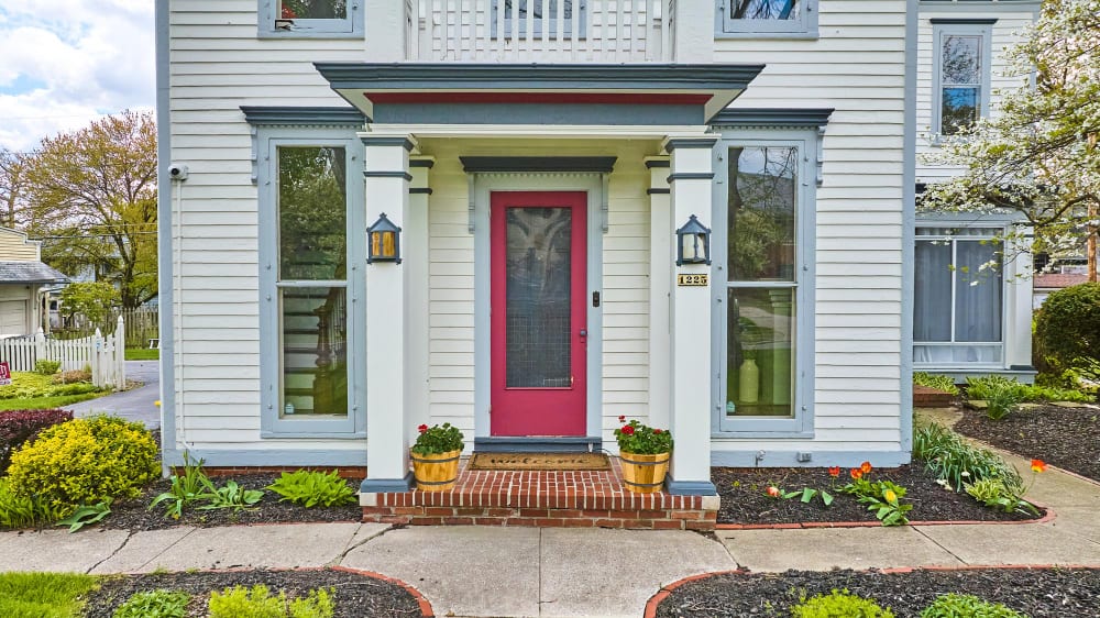 White house with a red front door, brick step, and flower pots