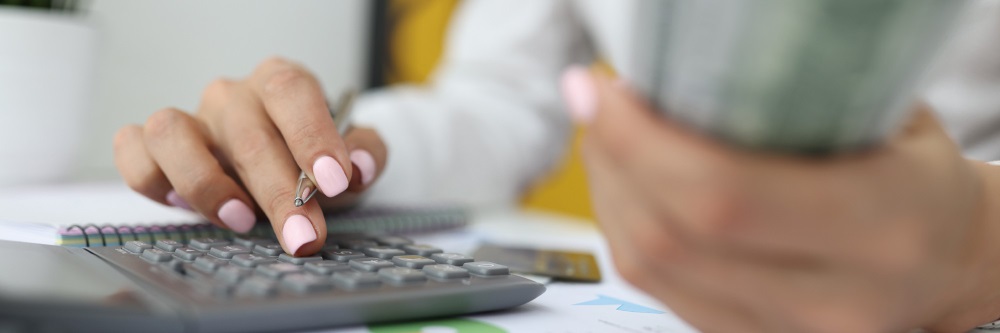 Hand with pink nails using a calculator while holding cash