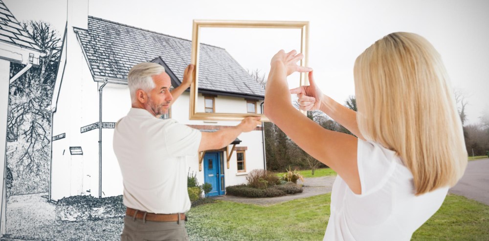 Couple holding an empty gold frame in front of a white house with a blue door