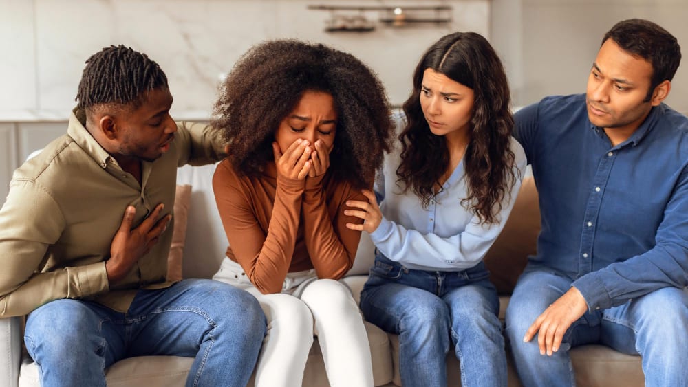 Four people on a sofa; a woman covering her face while others sit close