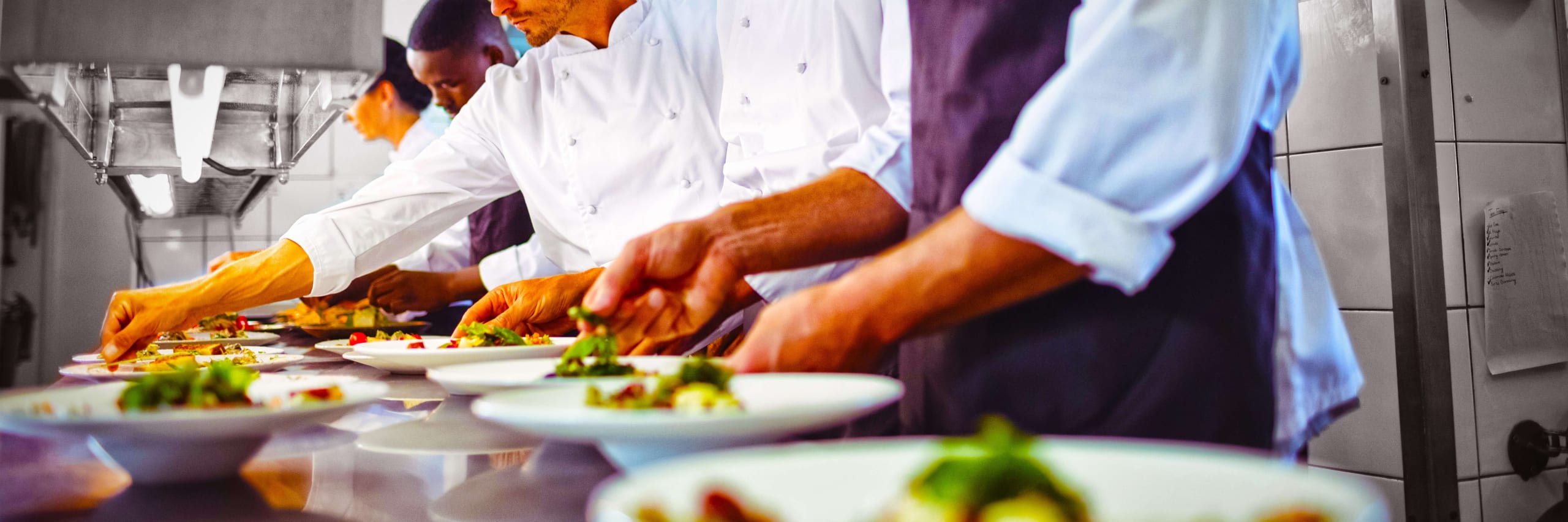 Chefs plating dishes on a restaurant kitchen pass