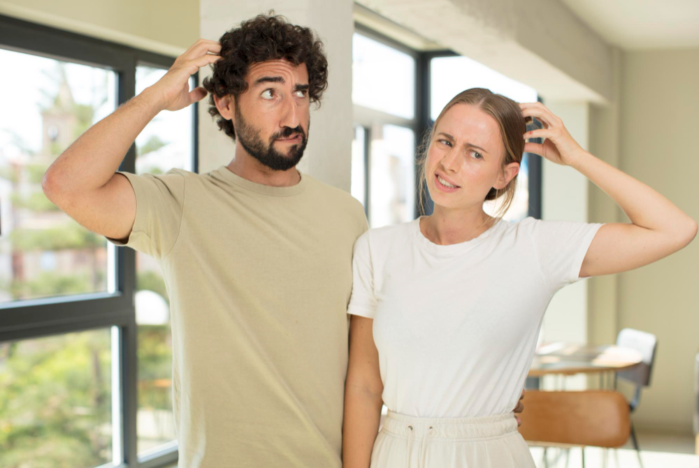 Couple scratching their heads in a bright room with large windows