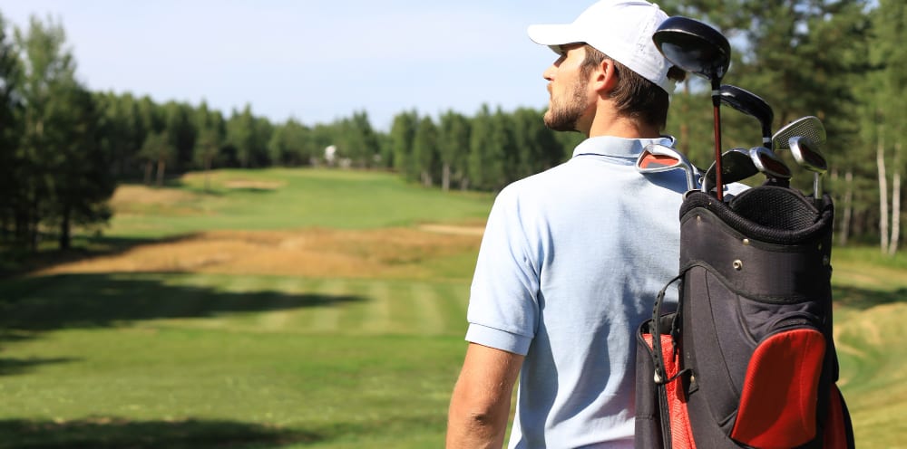Man with a golf bag looking down a tree-lined fairway
