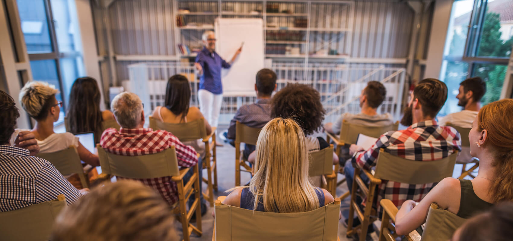 People in folding chairs watching a speaker at a whiteboard