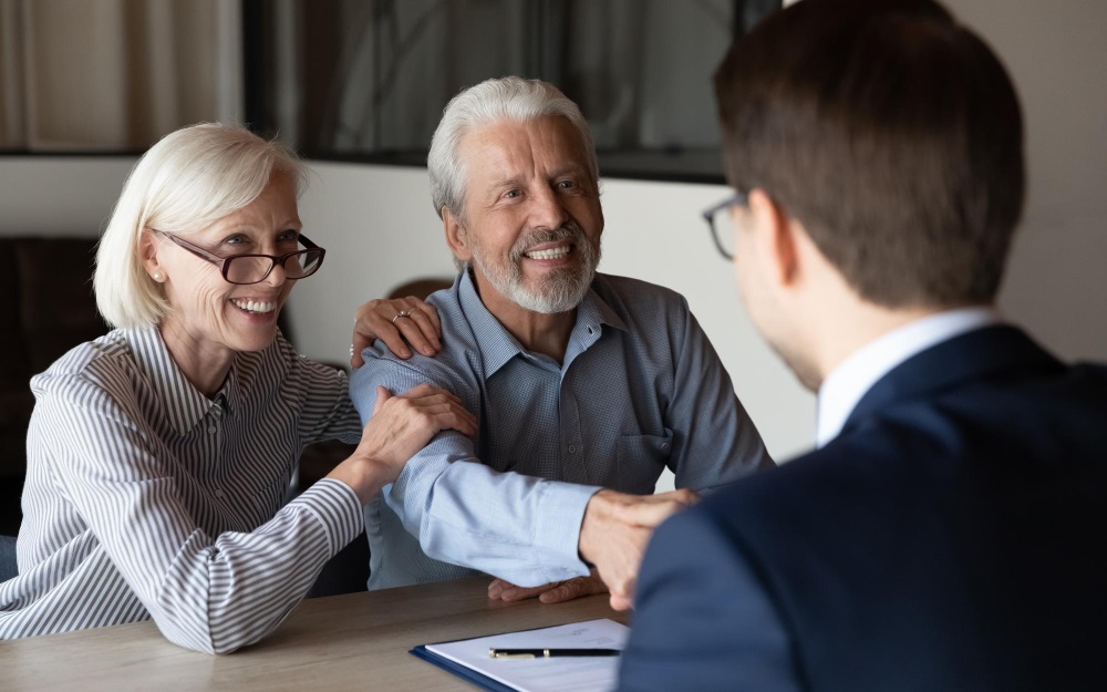 Older couple smiling while the man shakes hands with a professional