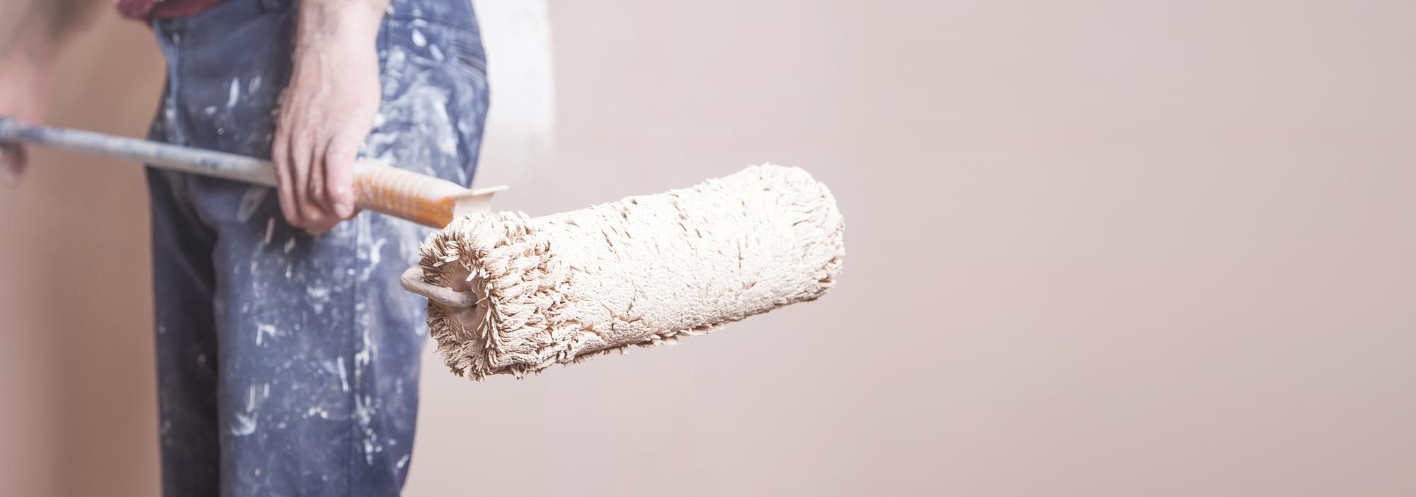 Person in paint-splattered jeans holding a paint roller