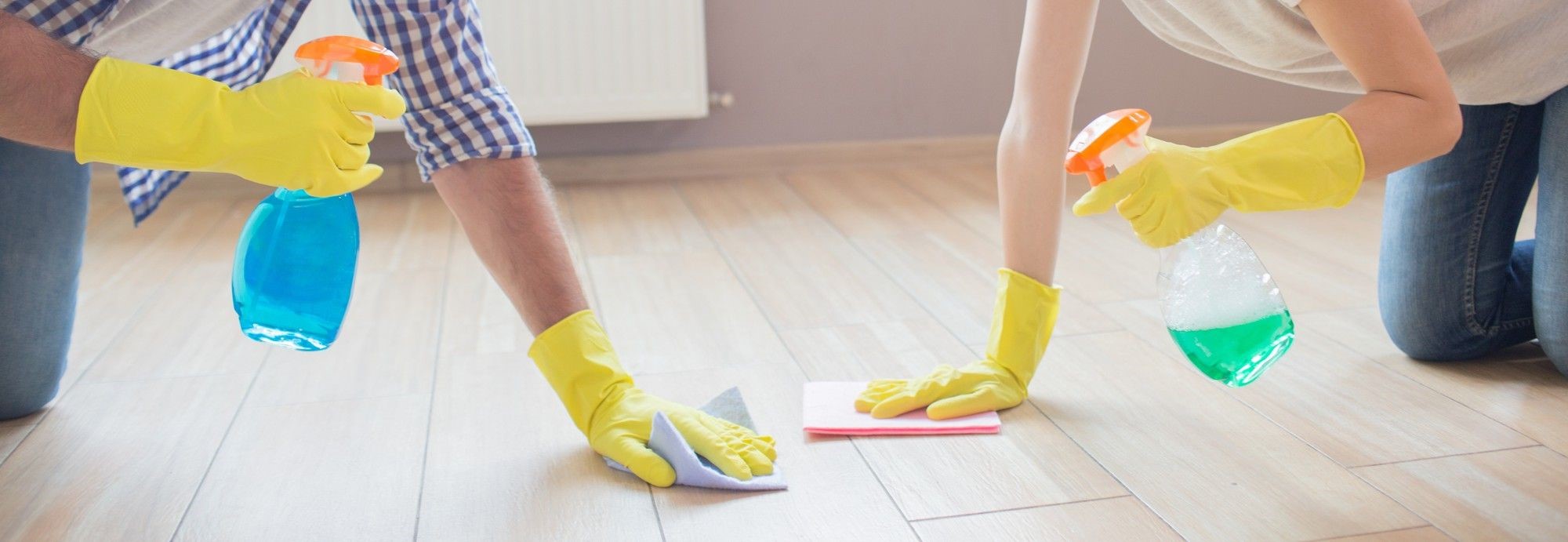 Two people in yellow gloves wiping a wood floor