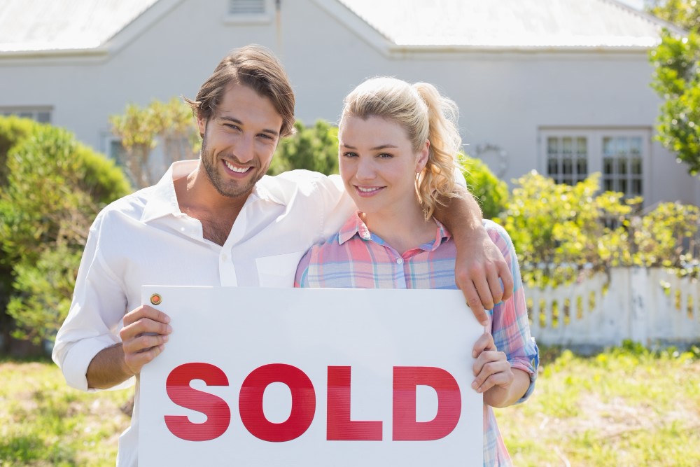 Couple holding a red Sold sign in front of a house