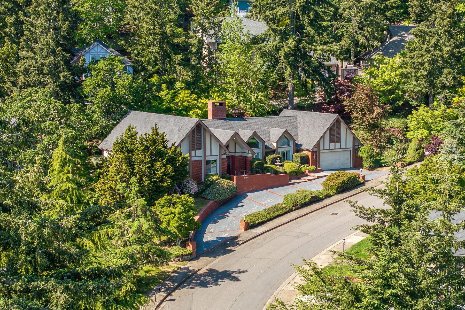 Aerial view of a hillside home with a brick drive and gabled roof in Eugene