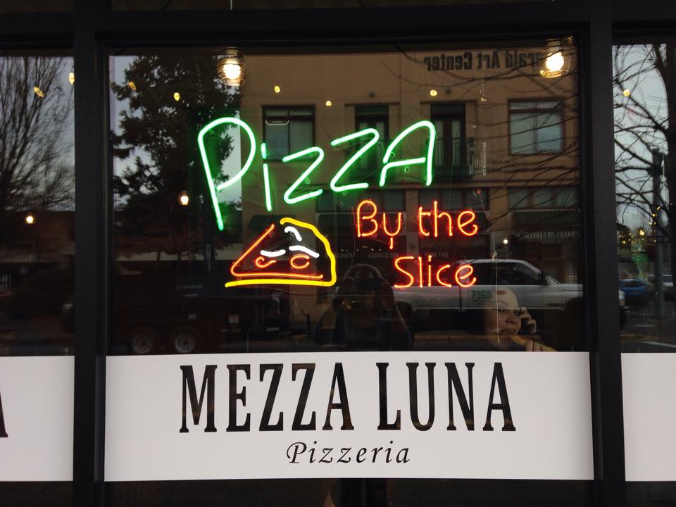 Mezza Luna Pizzeria window with Pizza By the Slice neon