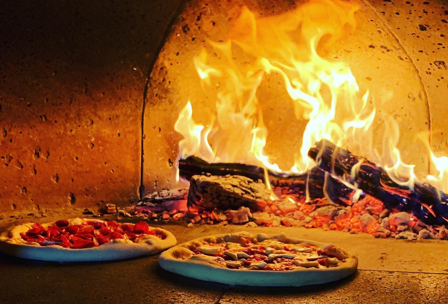 Two pizzas cooking in a wood-fired oven