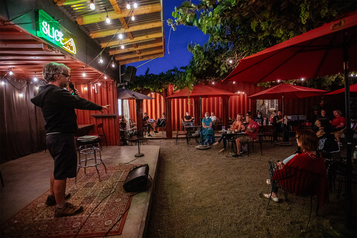 Performer on an outdoor patio under a Slice neon sign