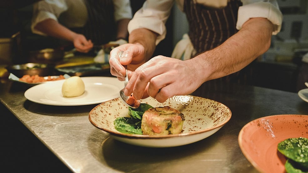 Chef plating a round dish with greens