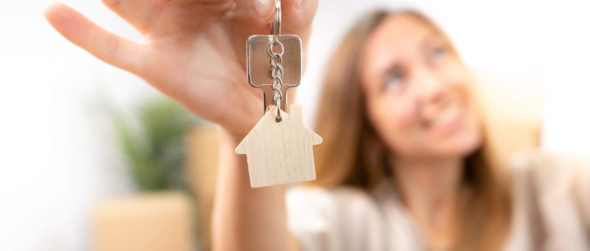 Woman holding out a key with a wooden house keychain