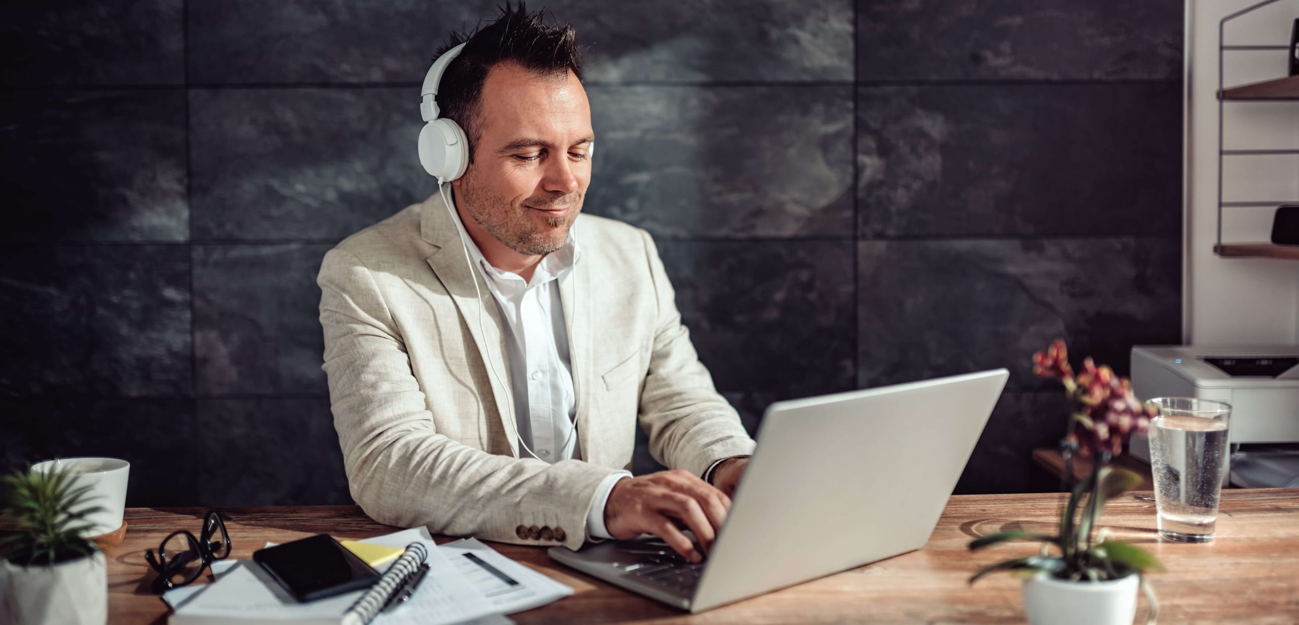 Man in headphones typing on a laptop at a wood desk