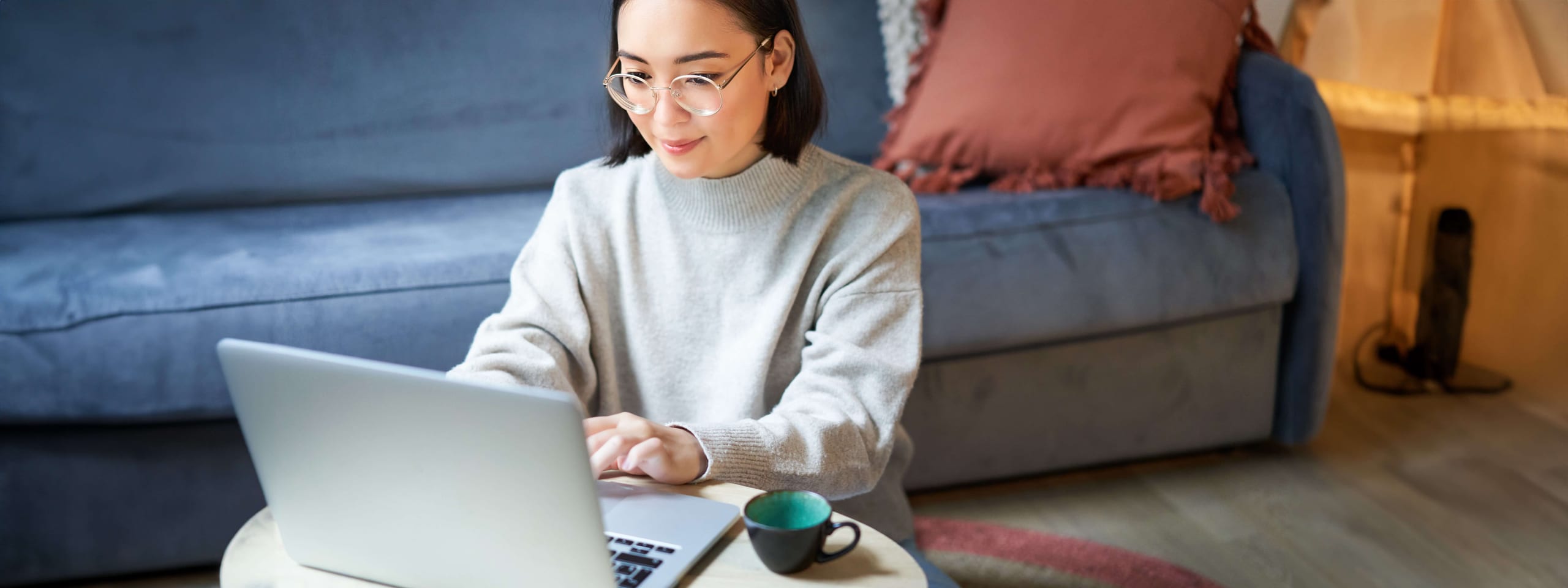 Woman with glasses working on a laptop at a low table