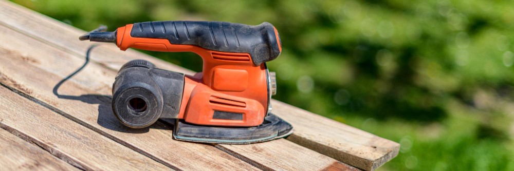 Orange orbital sander on weathered deck boards