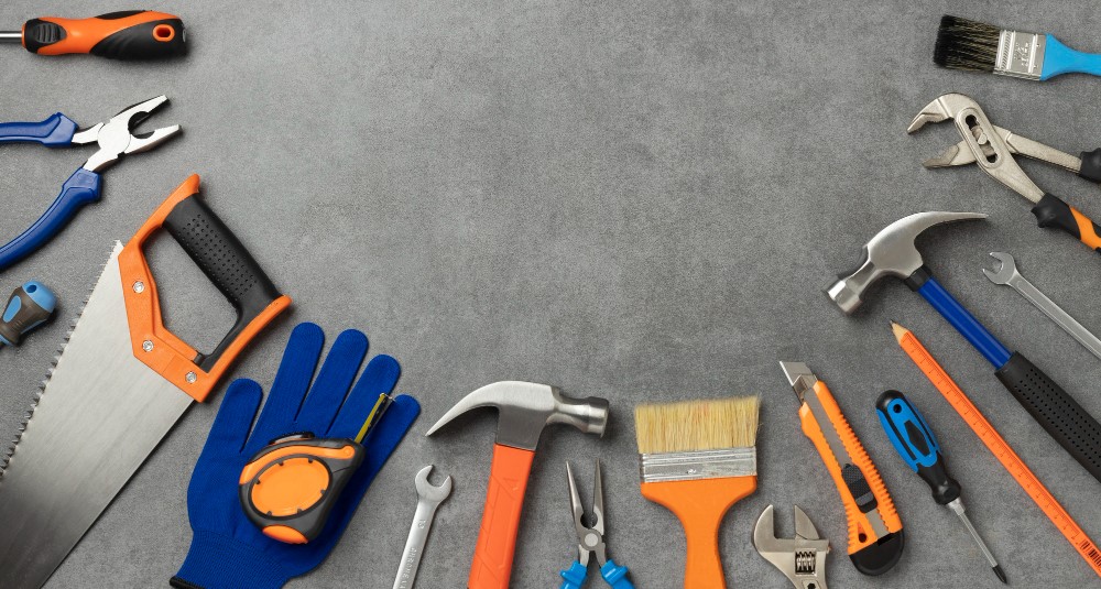 Hammers, saw, gloves, and paintbrushes on a gray table