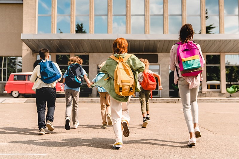 Children with backpacks running toward a school building