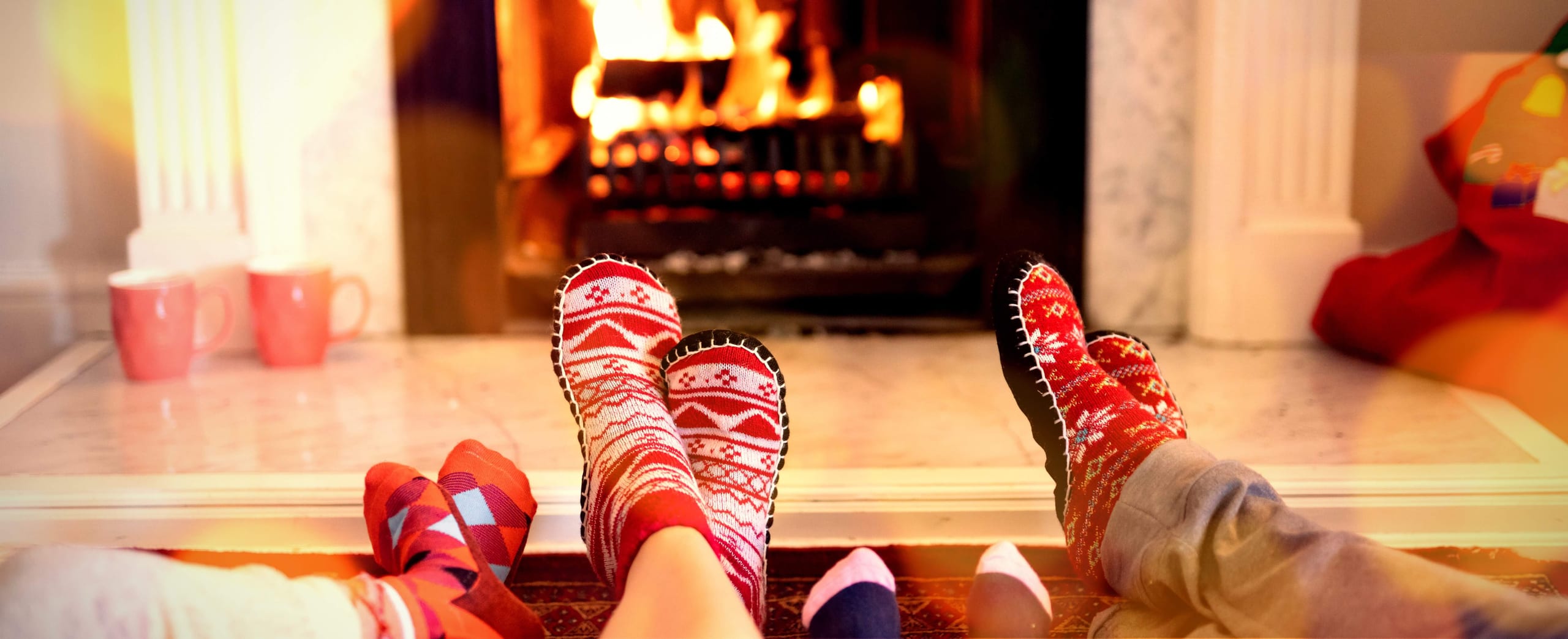 Socked feet by a fireplace with cocoa mugs