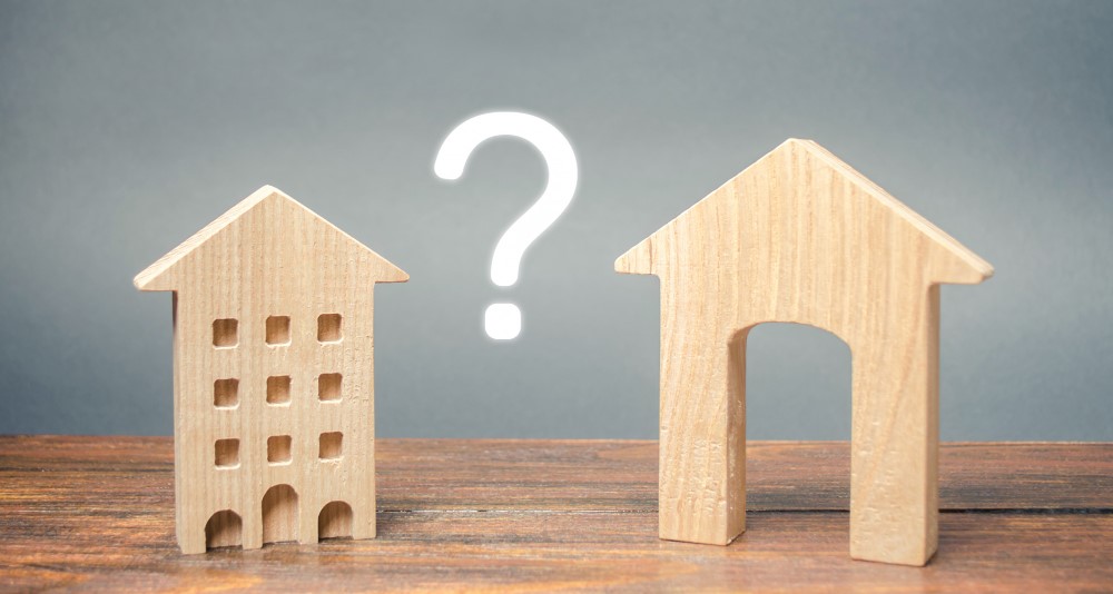 Wooden house and apartment models with a question mark between them