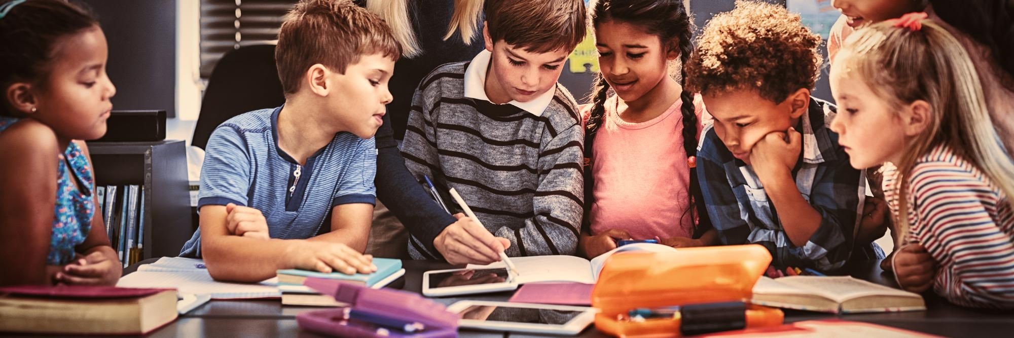 Schoolchildren gathered around a table with books and a tablet