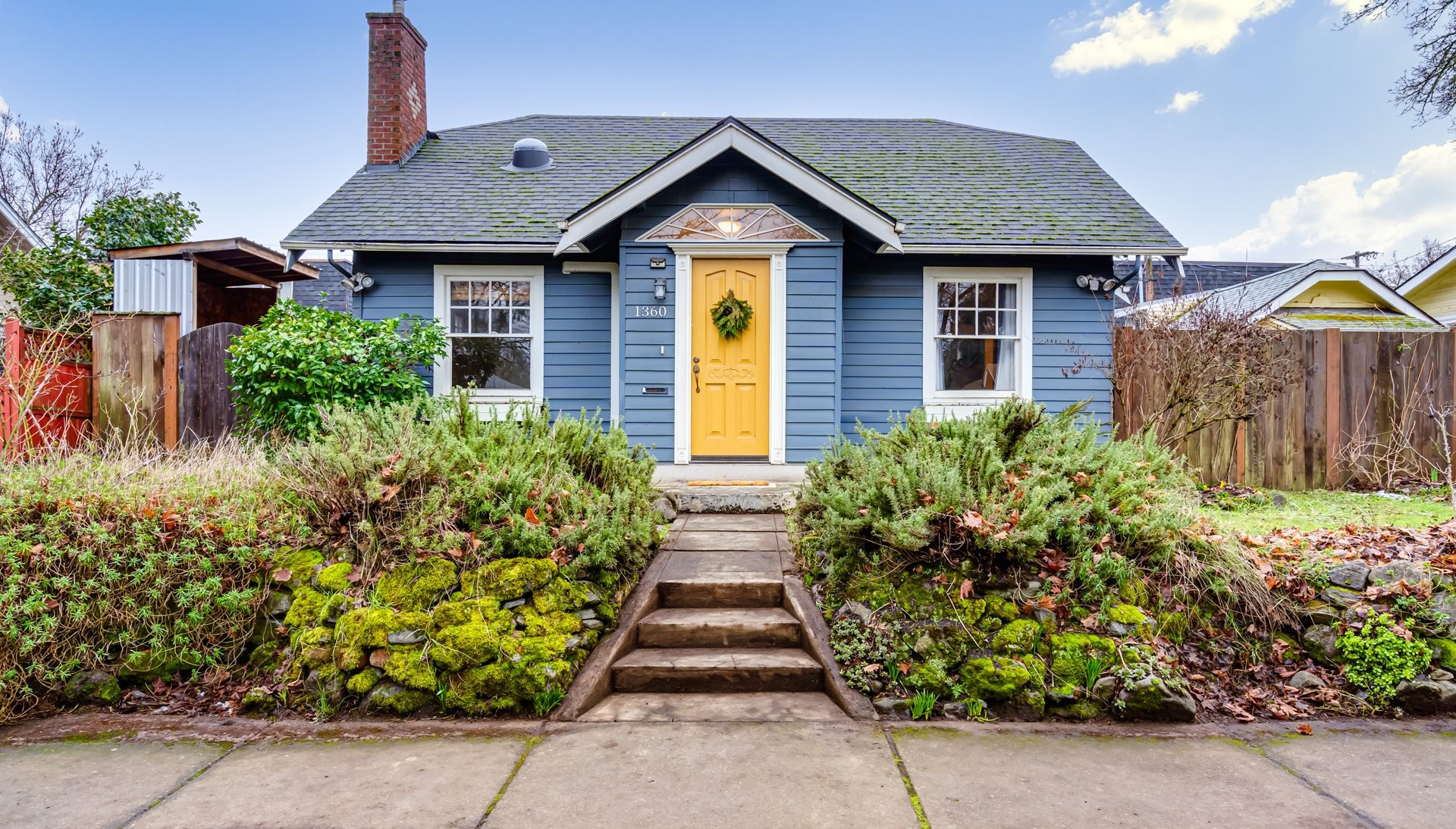Blue bungalow with a yellow door and mossy stone wall