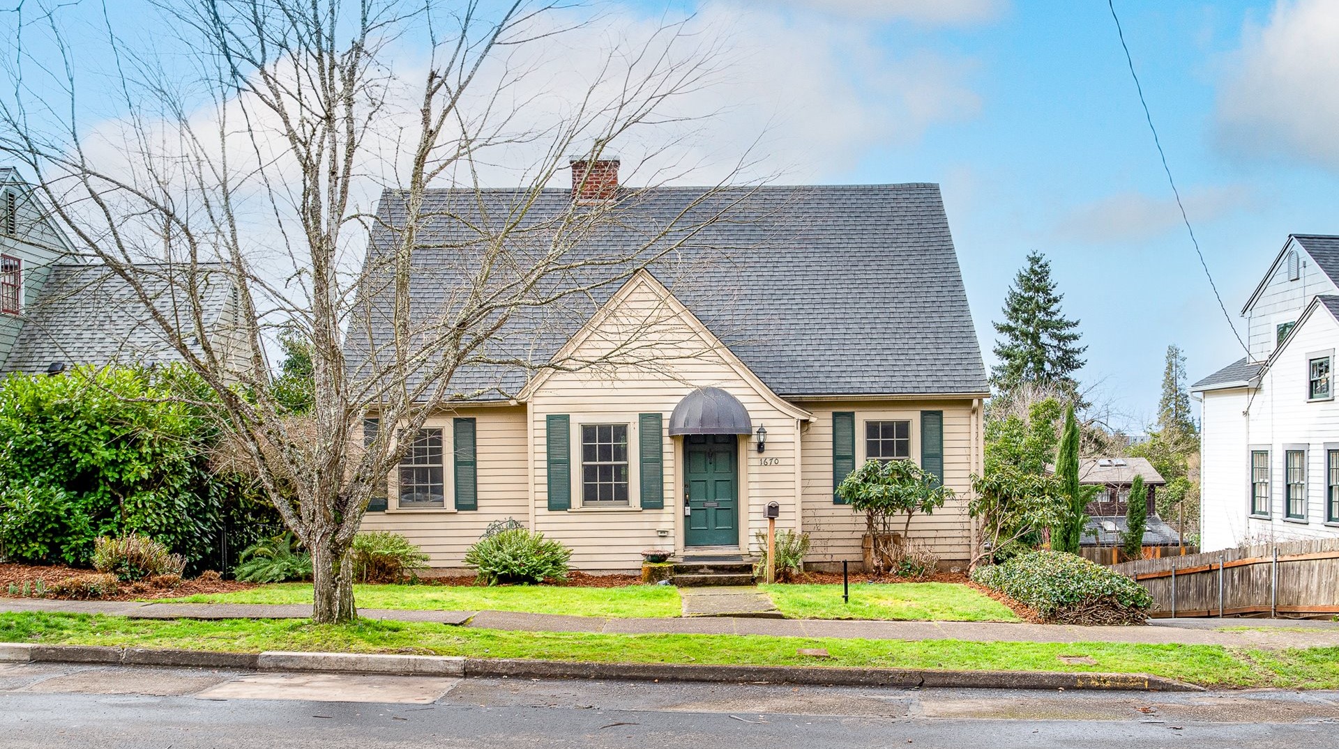 Beige cottage with green shutters and a rounded porch roof