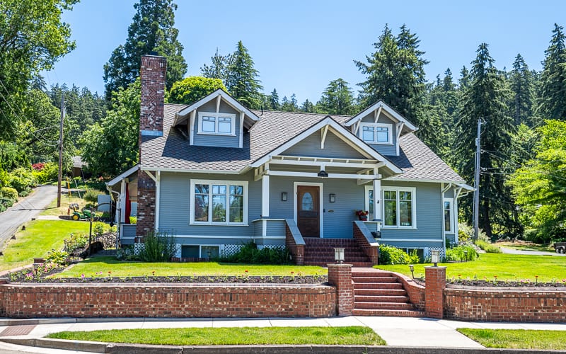 Gray Craftsman house with brick steps and a brick chimney