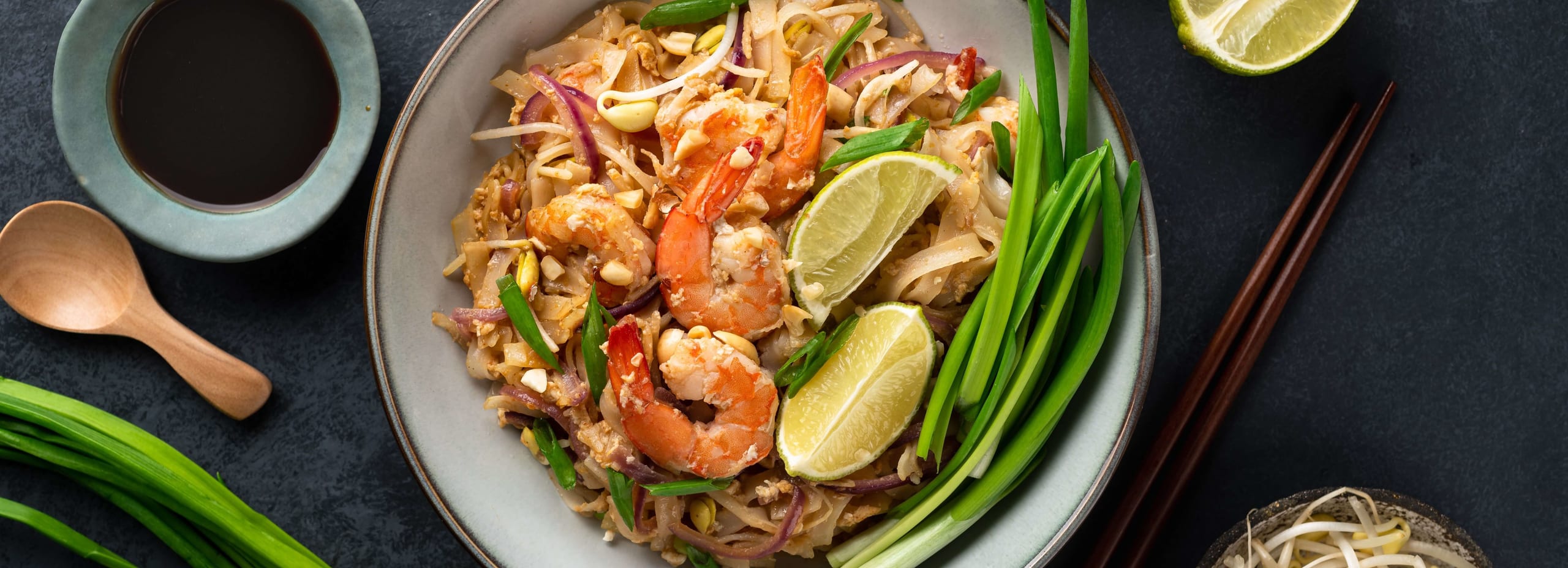 Bowl of shrimp pad thai with lime and green onion
