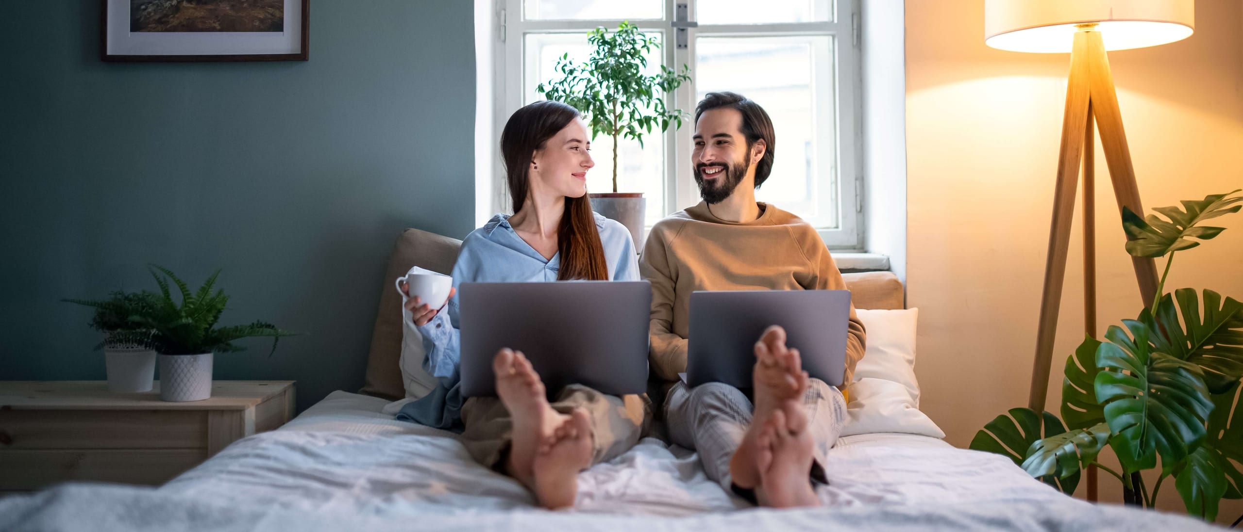 Couple sitting on a bed with laptops looking at each other
