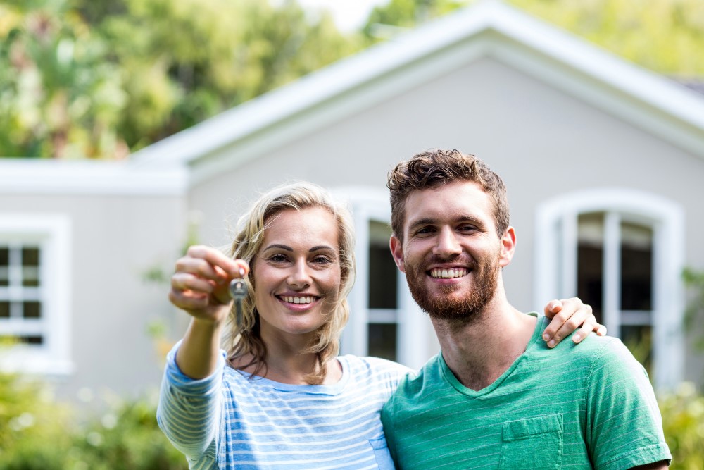 Smiling couple in front of a house, the woman holding out keys