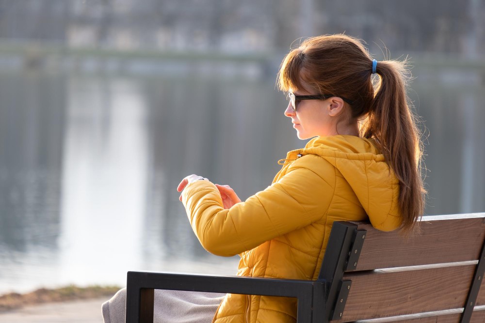 Woman in a yellow jacket on a park bench looking at her watch